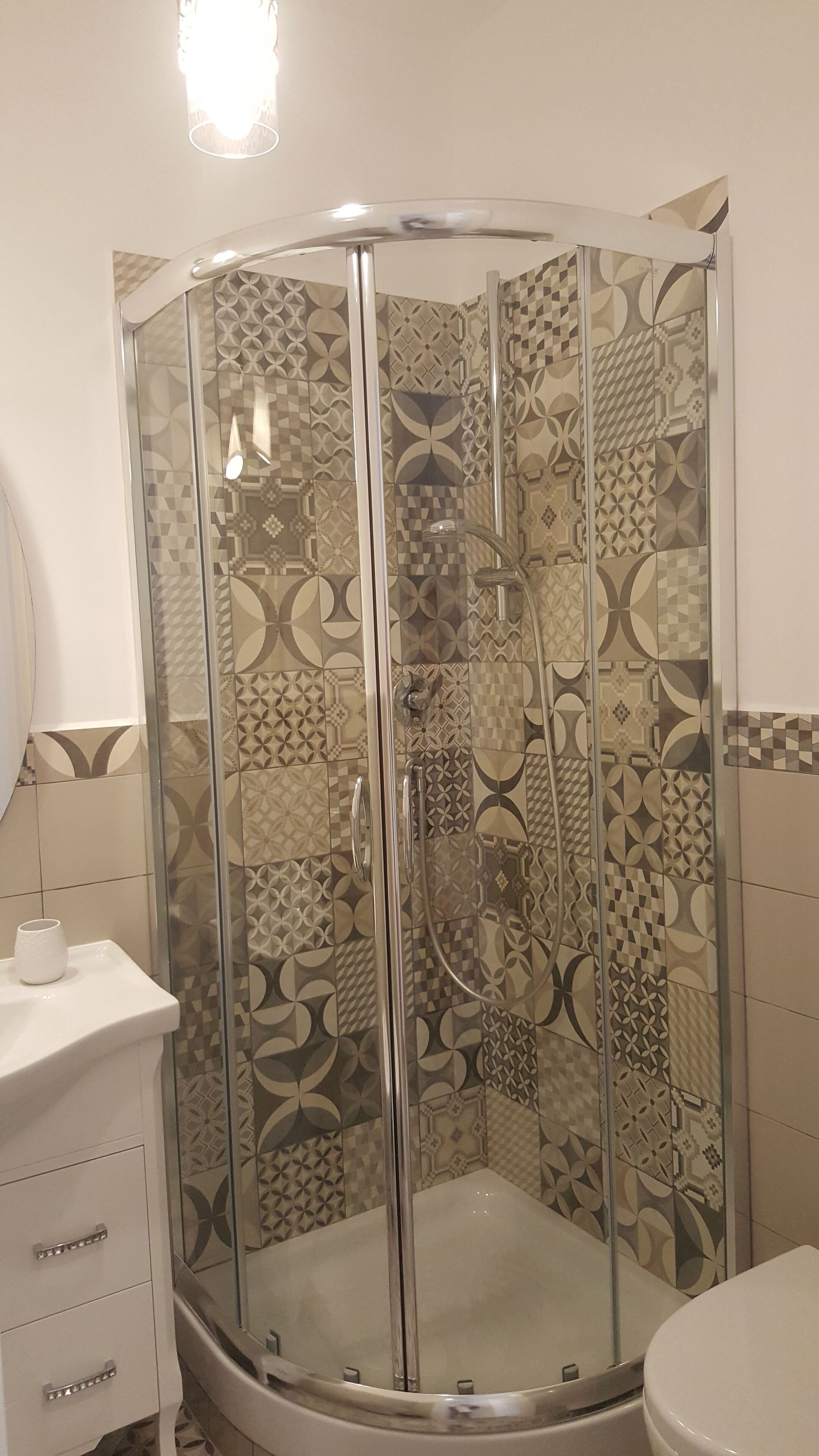 Zona de ducha con puerta de vidrio y pared con diseños geométricos.