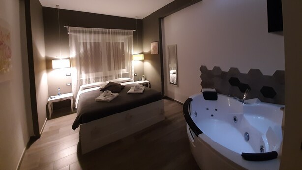 A modern hotel room with a large bed, a sitting area with a table and chairs, a bathroom with a bathtub, and a ceiling with recessed lighting. - Il Mare di Roma Luxury (Rome)