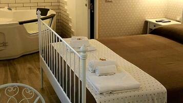 A hotel room with a white crib, a bed with a brown bedspread, a white table with a lace tablecloth, and a vase with flowers.