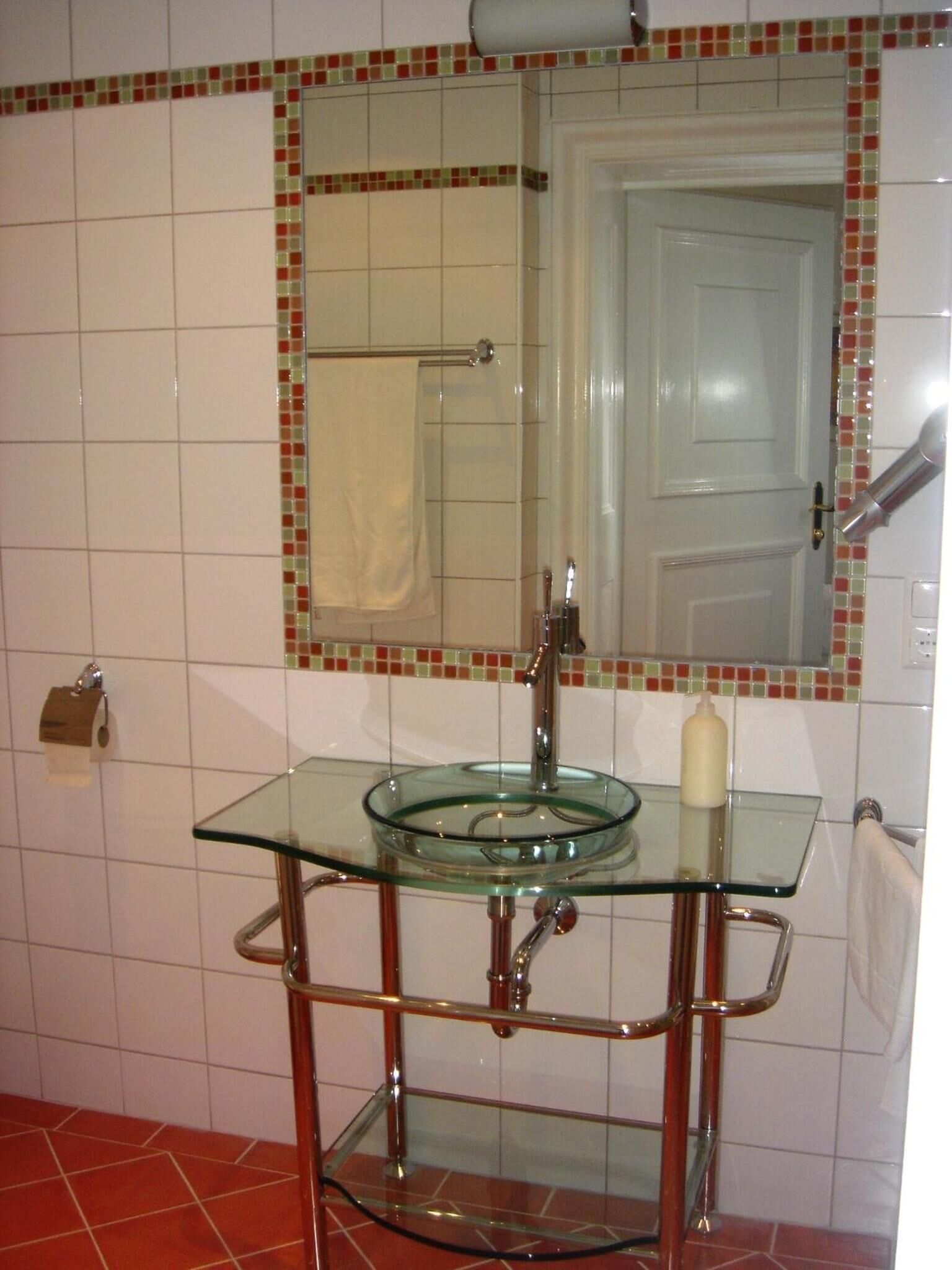 A bathroom with a glass sink, a mirror, and a towel rack.