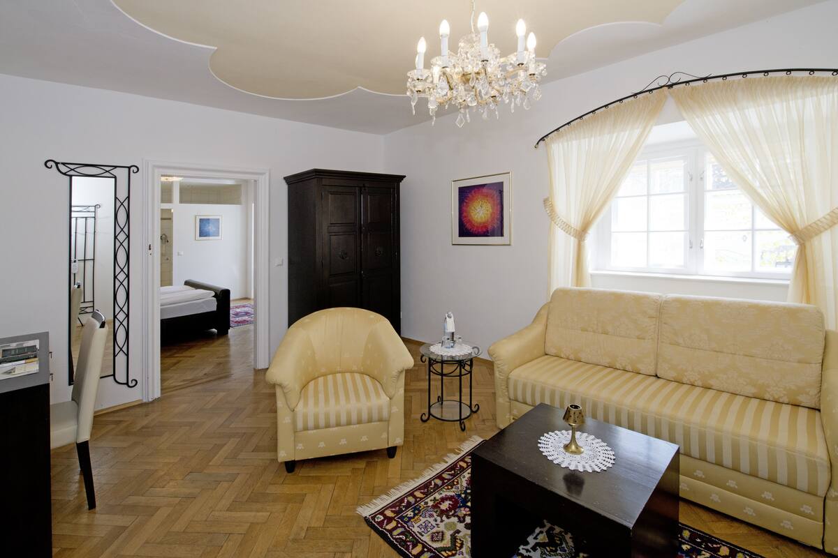 A living room with a sofa, armchairs, a chandelier, and a large window with curtains.