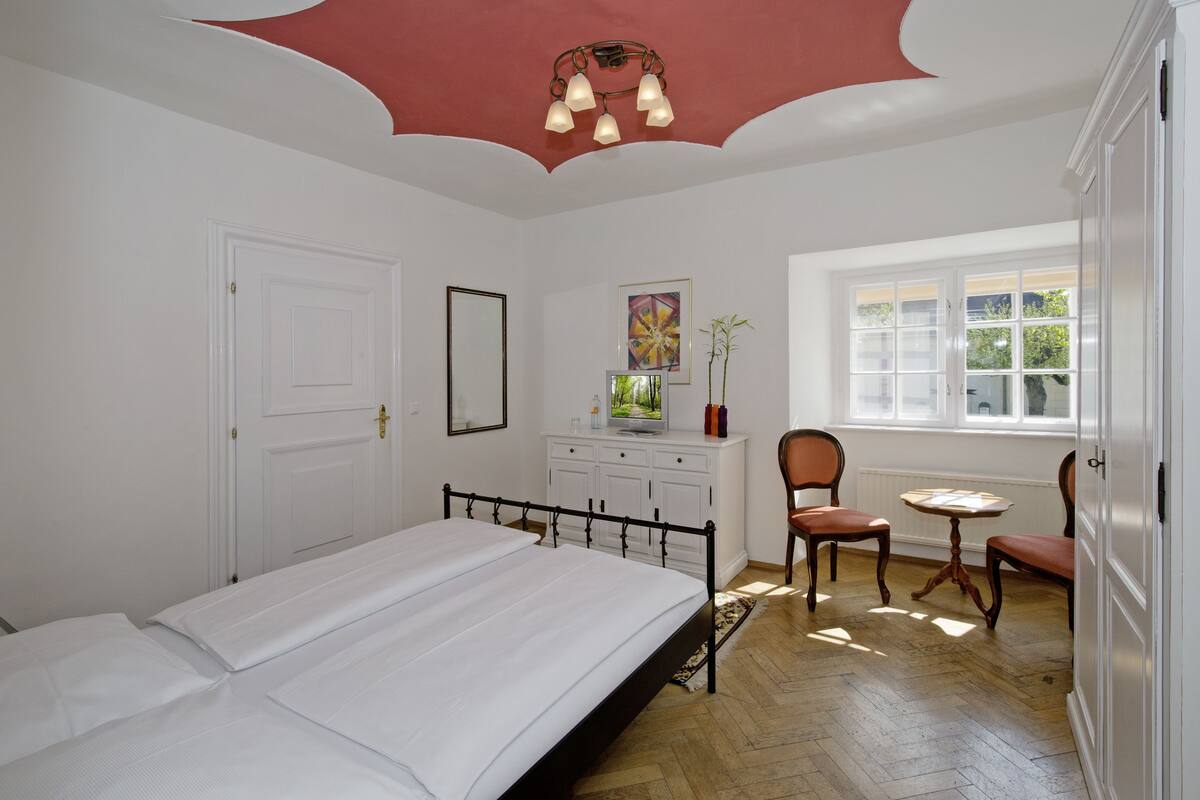 A bedroom with a bed, a desk, a chair, a window, and a radiator.