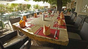 Un espacio de comedor al aire libre con mesas de piedra, sillas de mimbre y sombrillas.