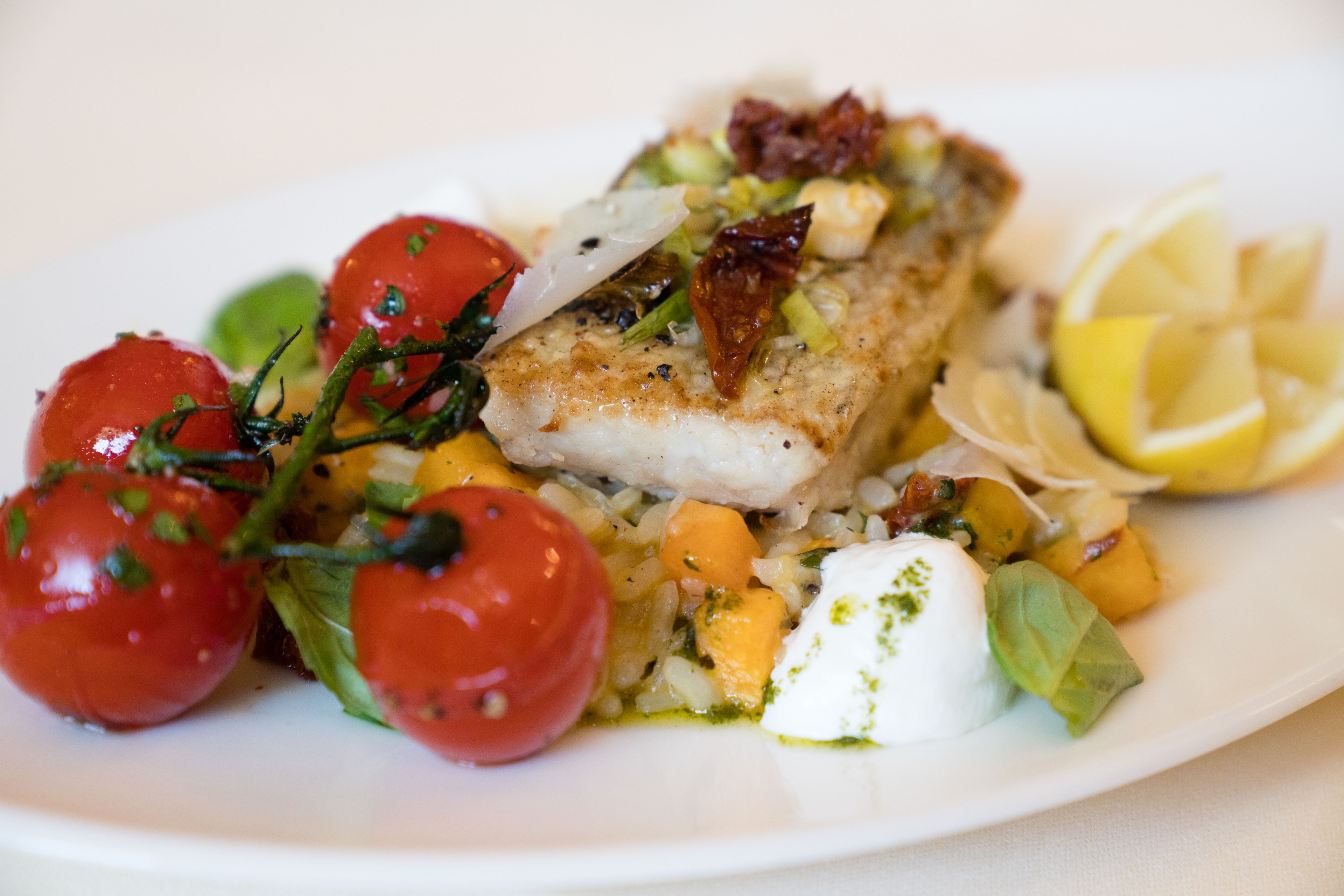 En tallerken mad med fisk, tomater og et stykke citron.