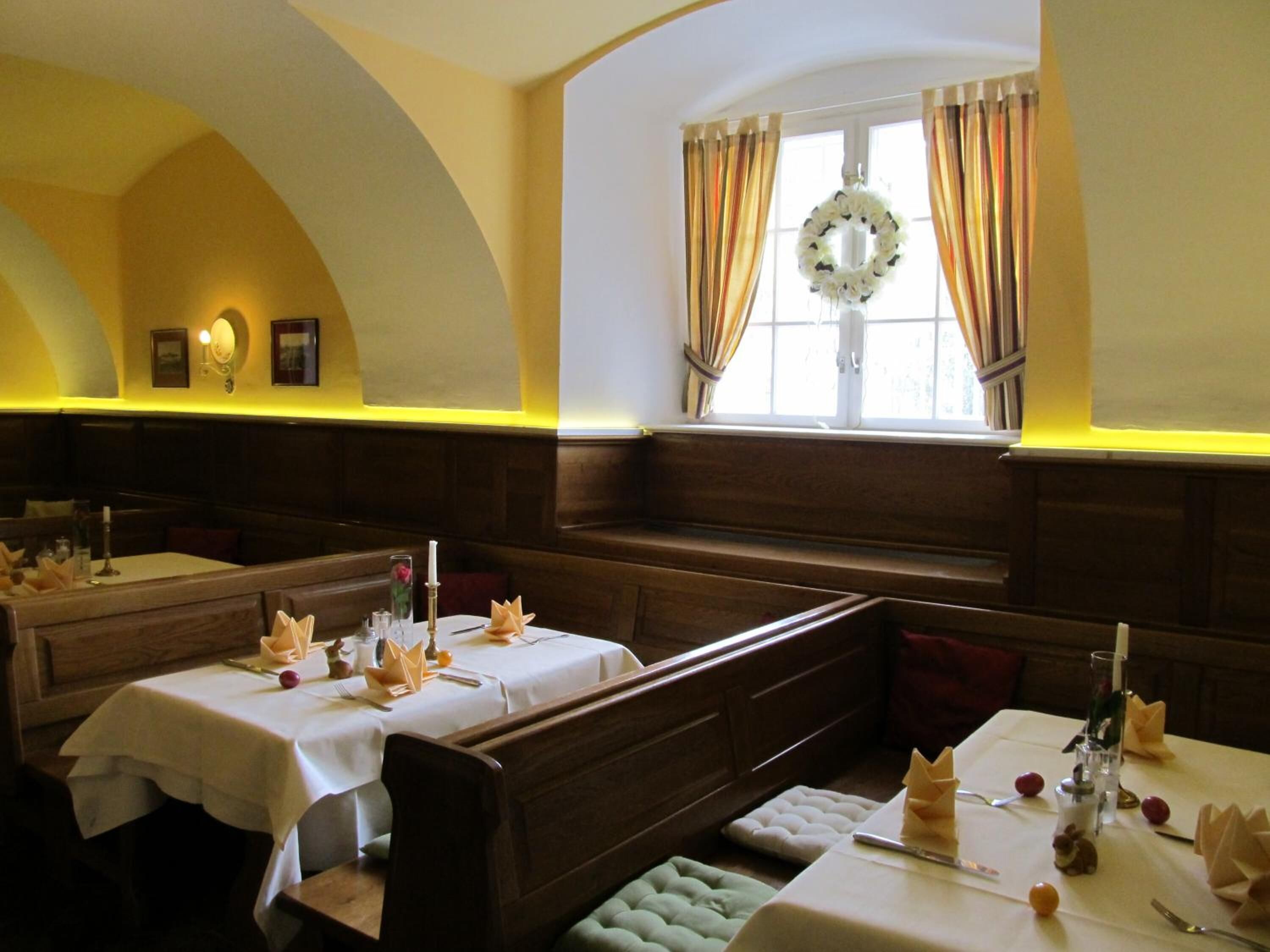Un restaurante con cabinas de madera con respaldo alto, manteles blancos y un adorno de guirnalda en la ventana.