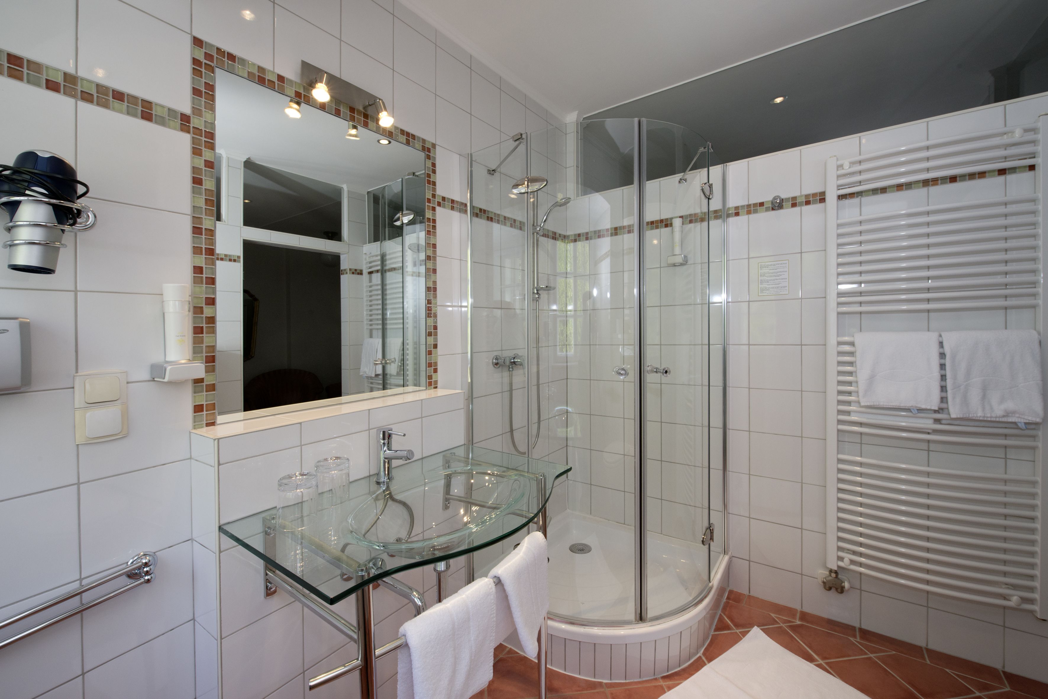 A modern bathroom with a glass shower enclosure, a glass sink, and a white tiled floor.