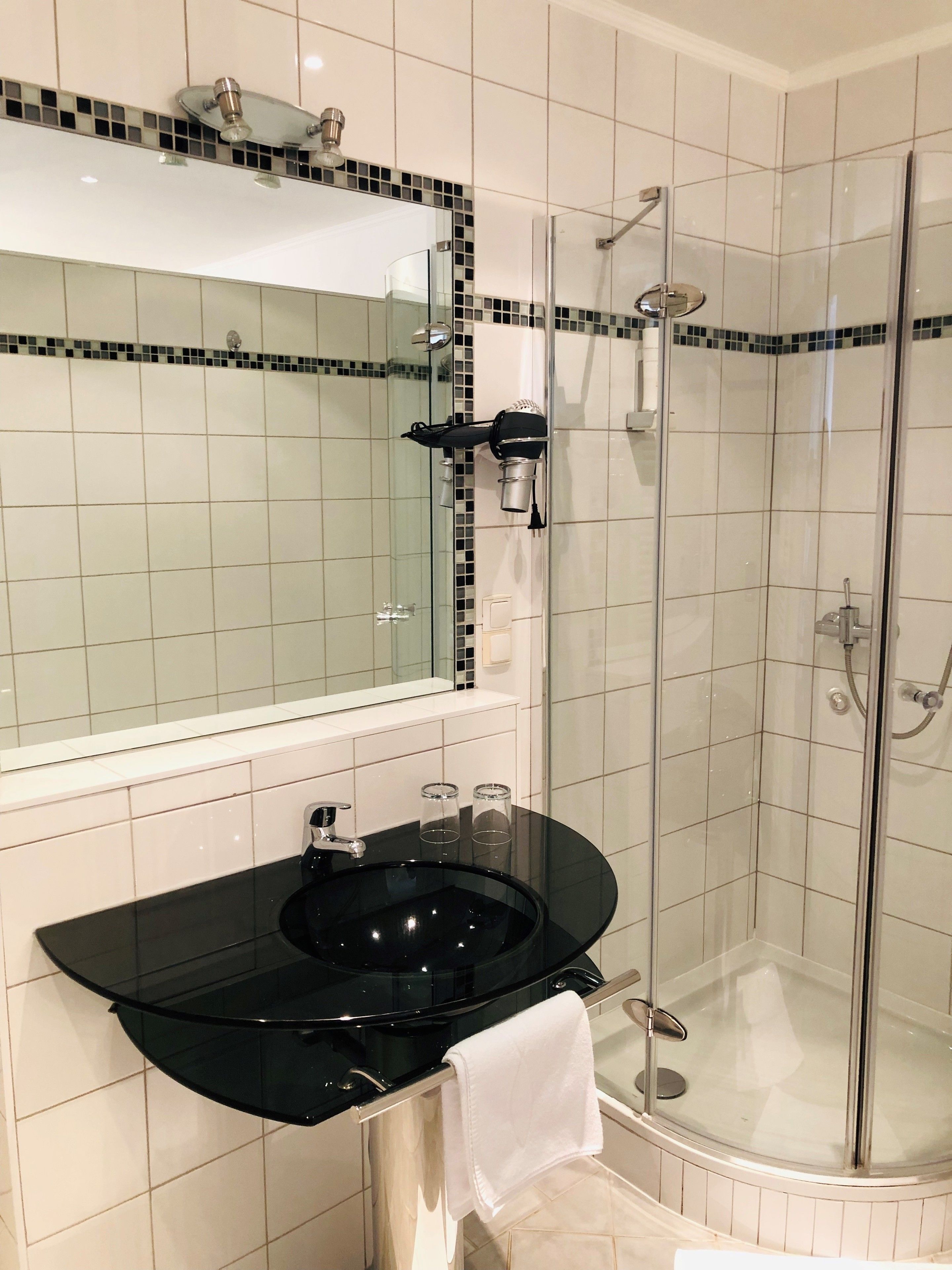 Un baño con un lavabo negro, un espejo, una cabina de ducha de cristal y una pared con azulejos.