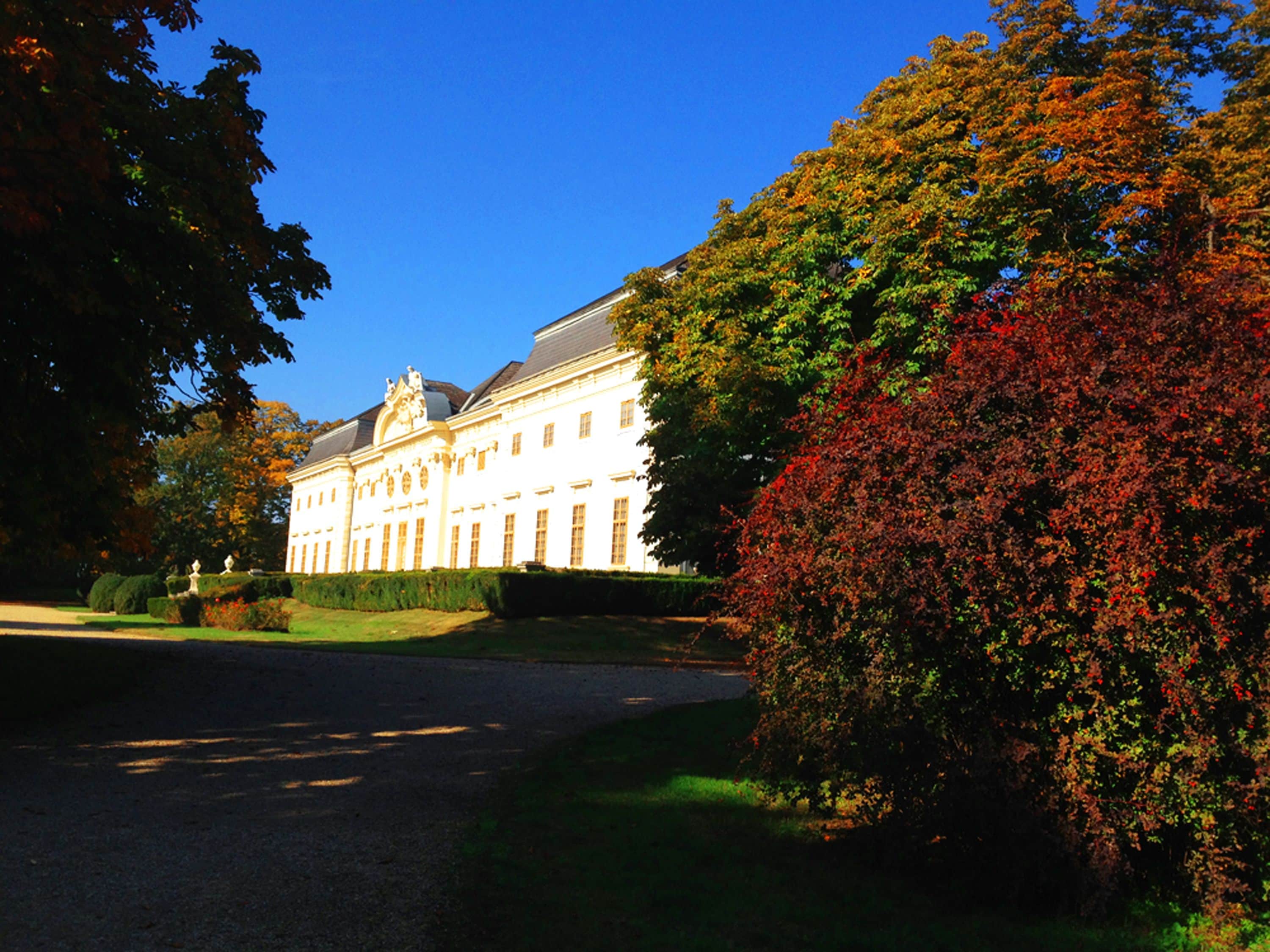 Ein großes, klassizistisches Gebäude mit symmetrischer Architektur, einem gepflegten Rasen und blauem Himmel.