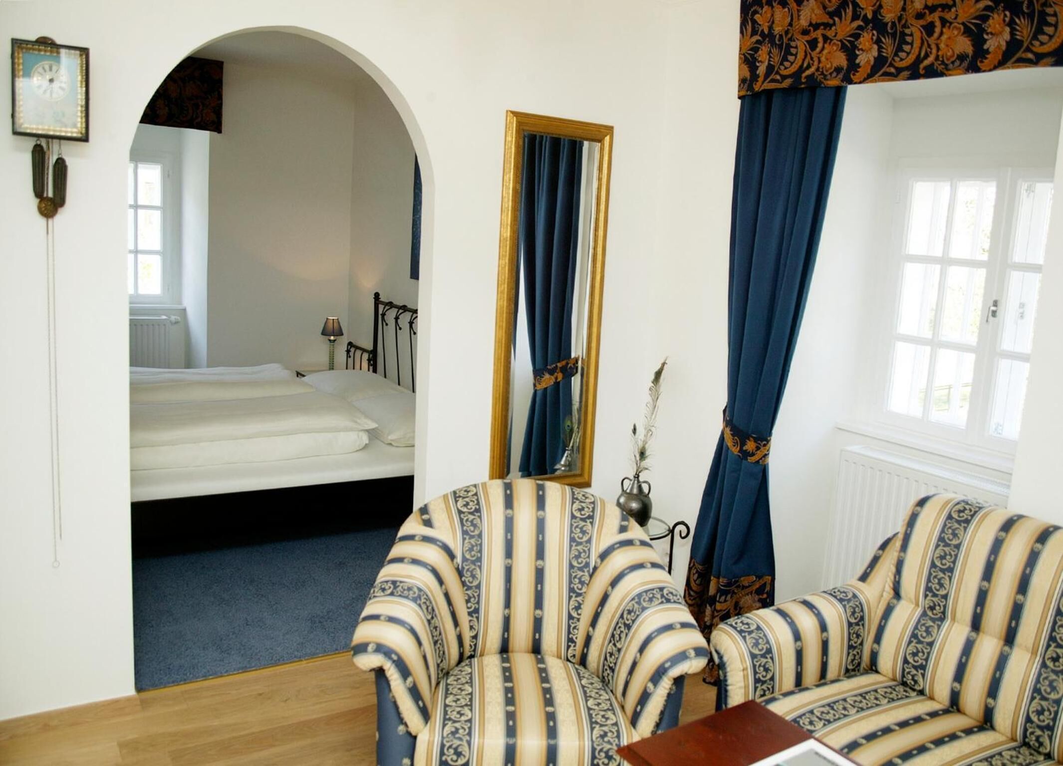 Una habitación con cama, sofá, espejo y ventana con cortinas.