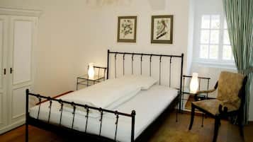 A bedroom with a four-poster bed, two bedside tables with lamps, a chair, and two framed bird paintings on the wall.