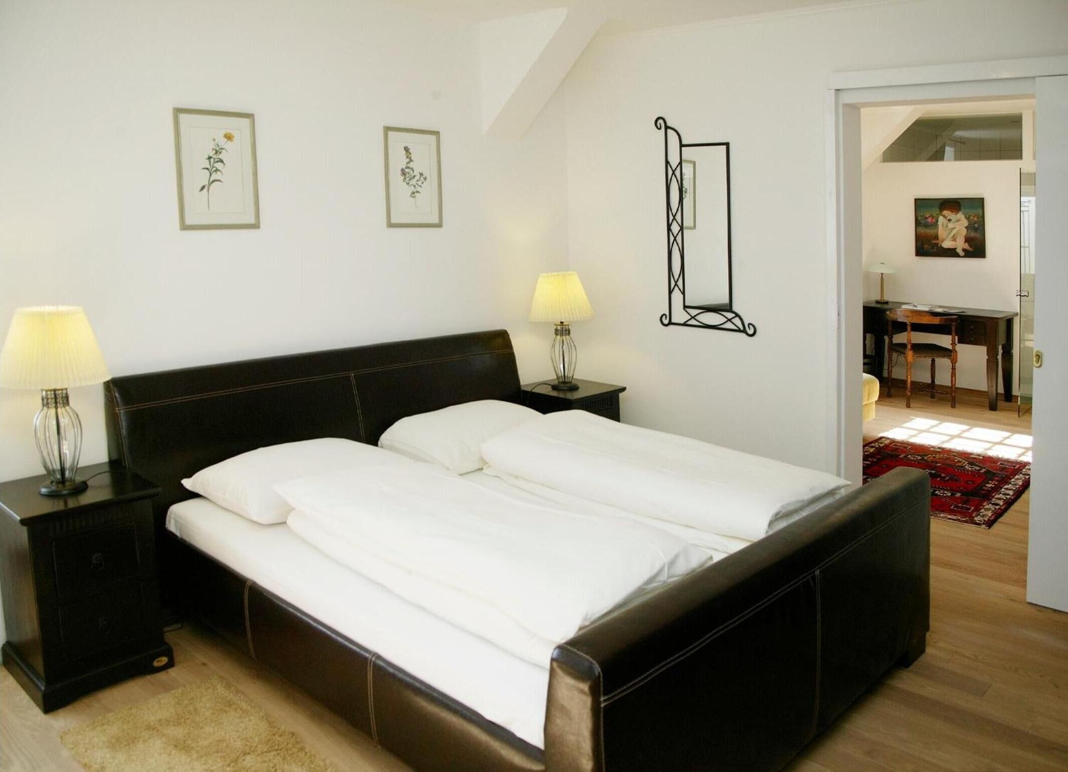 Un dormitorio con una cama grande, dos mesitas de noche con lámparas e impresiones botánicas enmarcadas en la pared.
