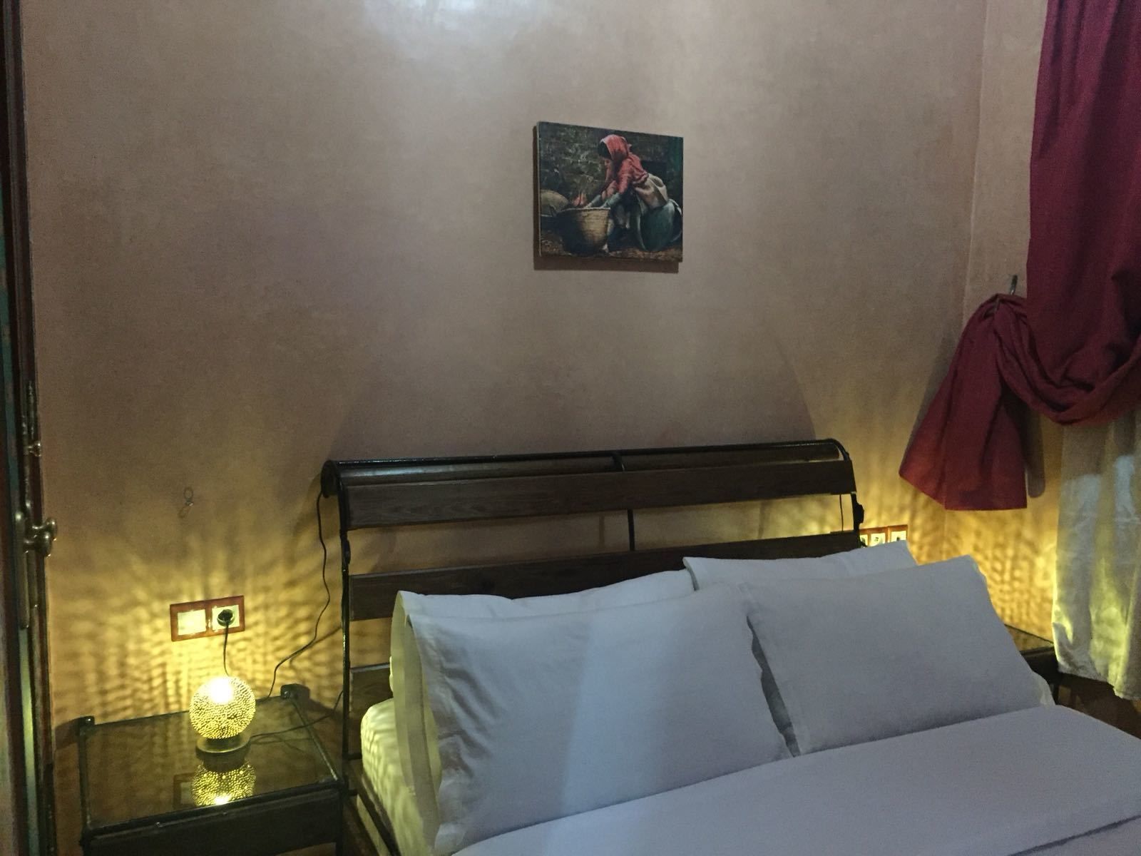 Un dormitorio con cabecera de madera, una cama individual con ropa blanca, una mesita de noche con lámpara y un cuadro en la pared.
