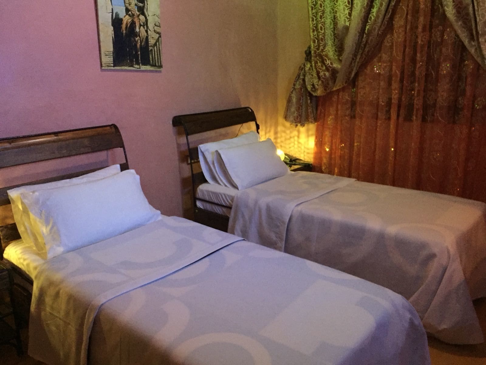A room with two single beds, a wooden headboard, a wall-mounted picture, and a curtain.