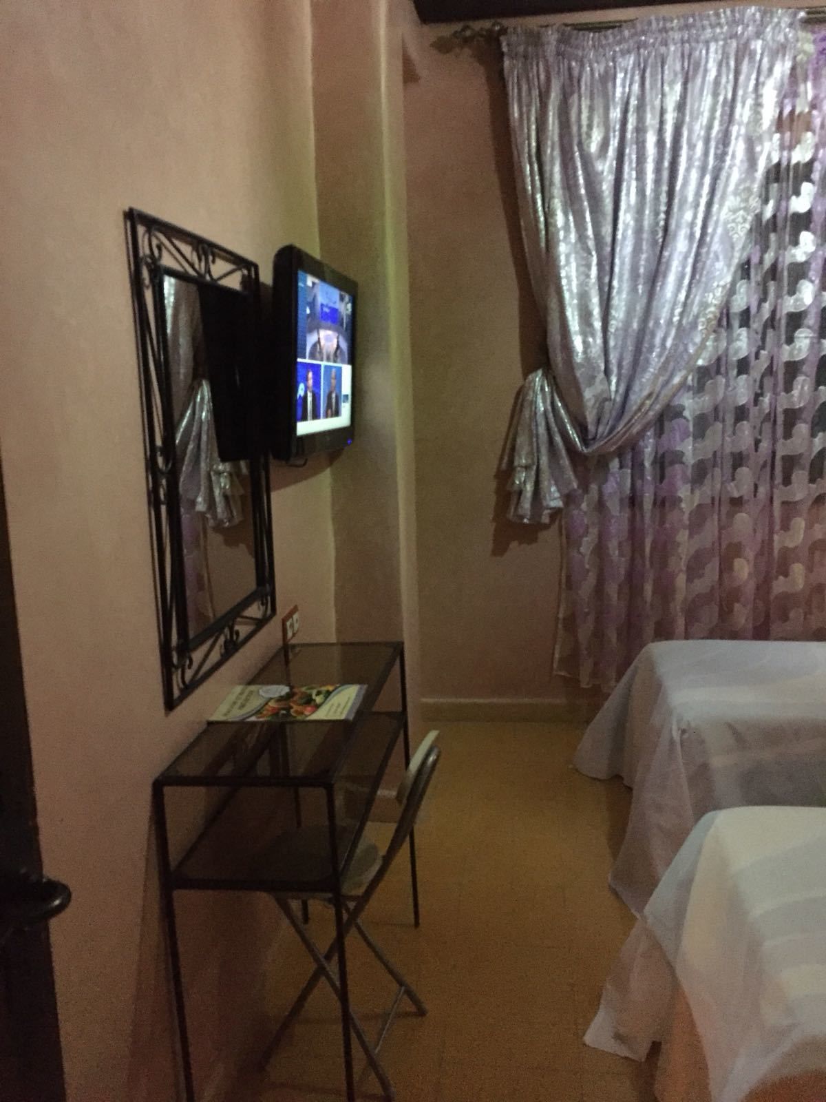 A hotel room with a television mounted on the wall, a small table with a magazine, and two beds with white linens.