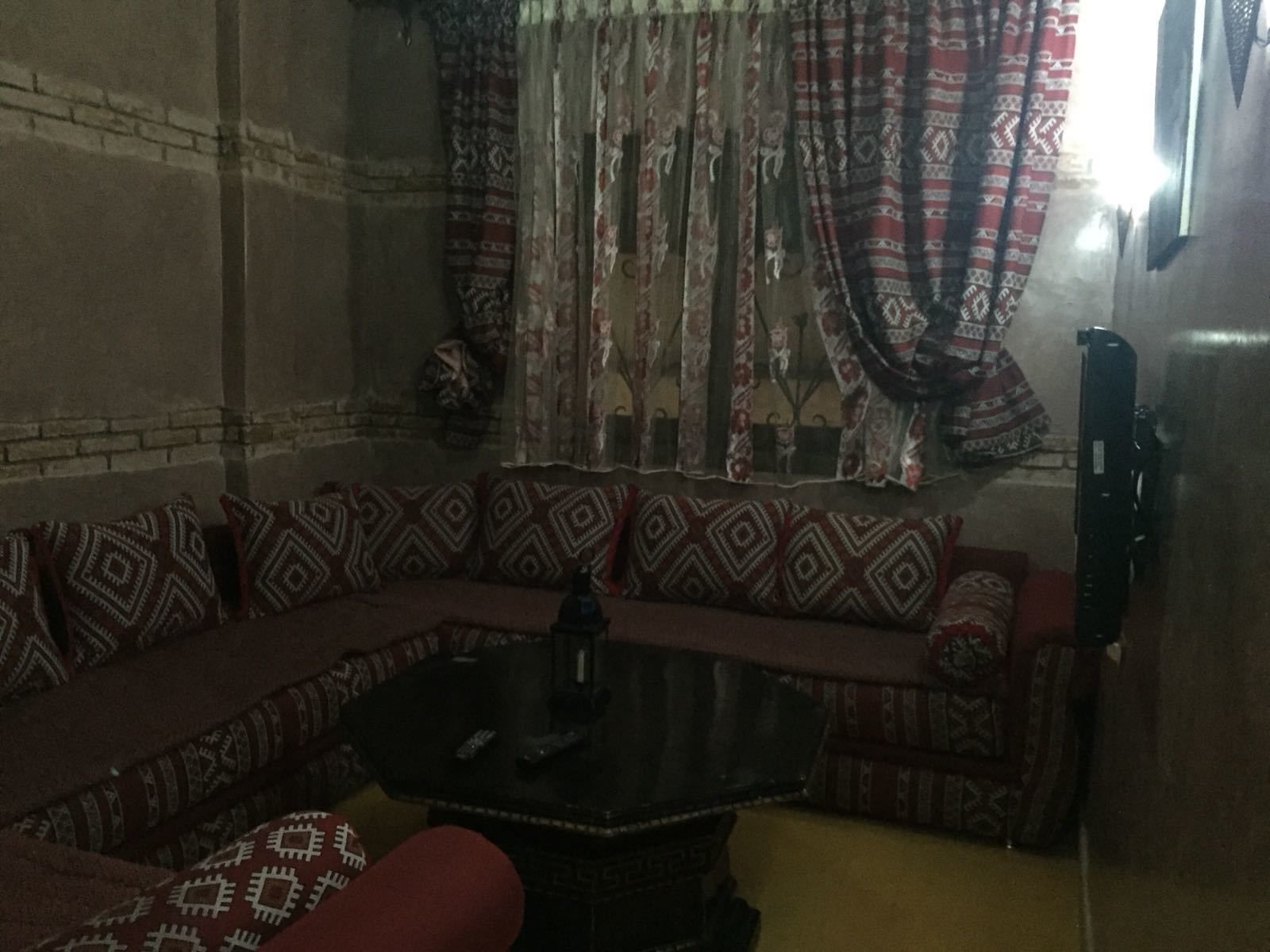 Una habitación con poca luz, un sofá estampado, una mesita y un cortinaje de diseño tradicional.