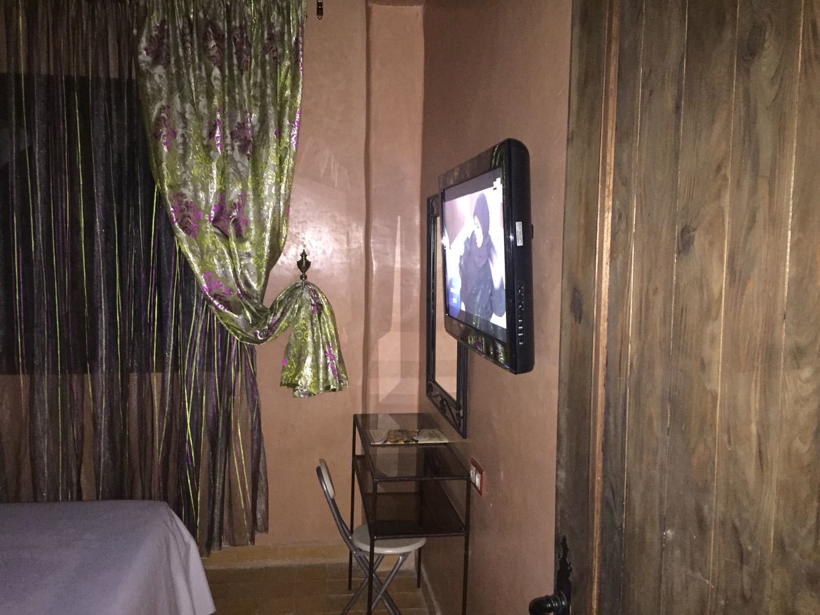 A hotel room with a bed, a television mounted on the wall, a small table, and a chair.