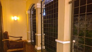 Un pasillo con suelo de baldosas, una silla de madera y ventanas con rejas y molduras blancas.