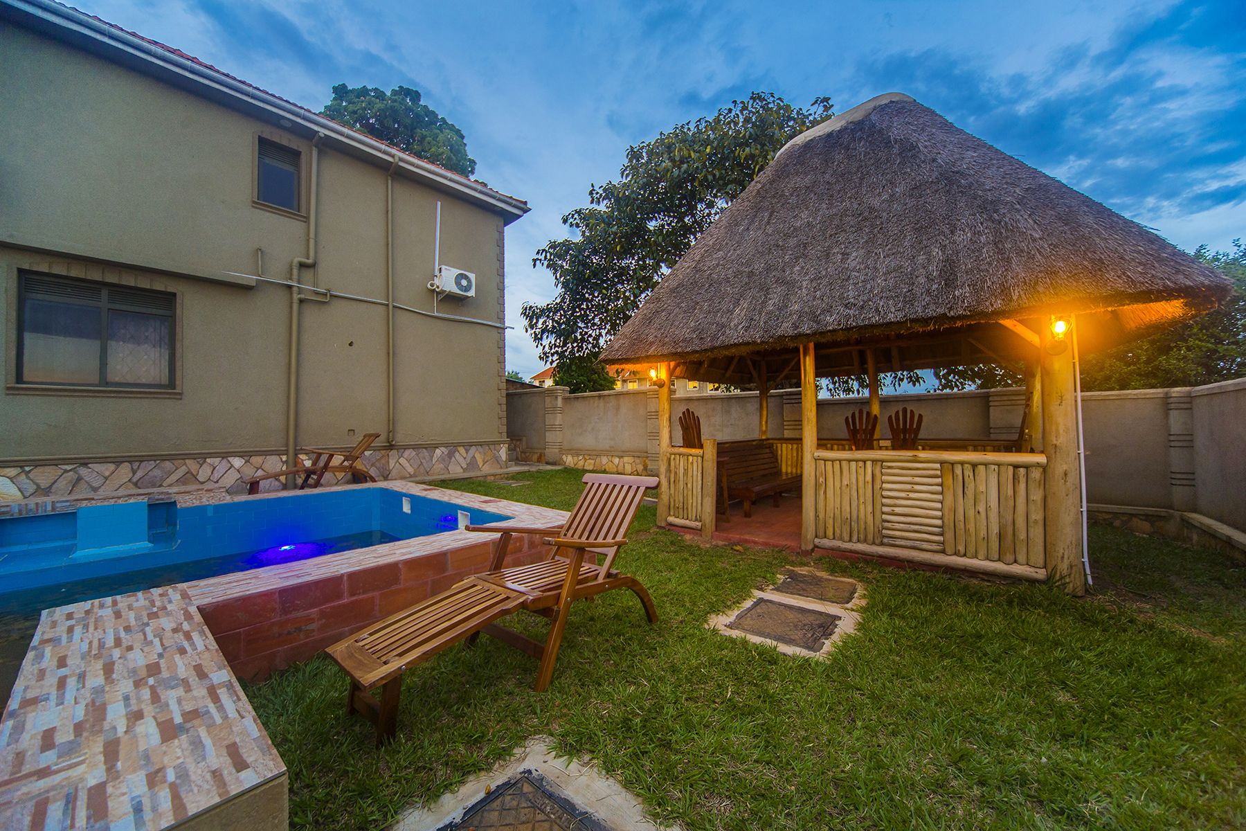 A backyard with a swimming pool, a wooden deck, and a thatched-roof gazebo.