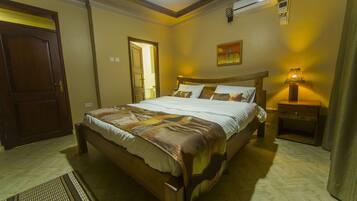A hotel room with a large bed, a bedside table with a lamp, a painting on the wall, and a door.