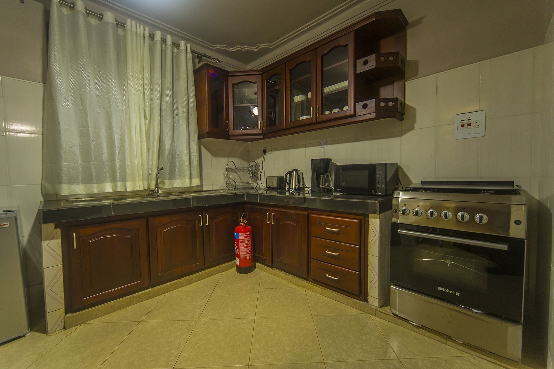 Una cocina con gabinetes de madera, estufa a gas, microondas y extintor.