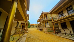 A courtyard with a cobblestone path, buildings with balconies, and a clear sky. - Victoria Breeze Hotel Apartment (Iganga)