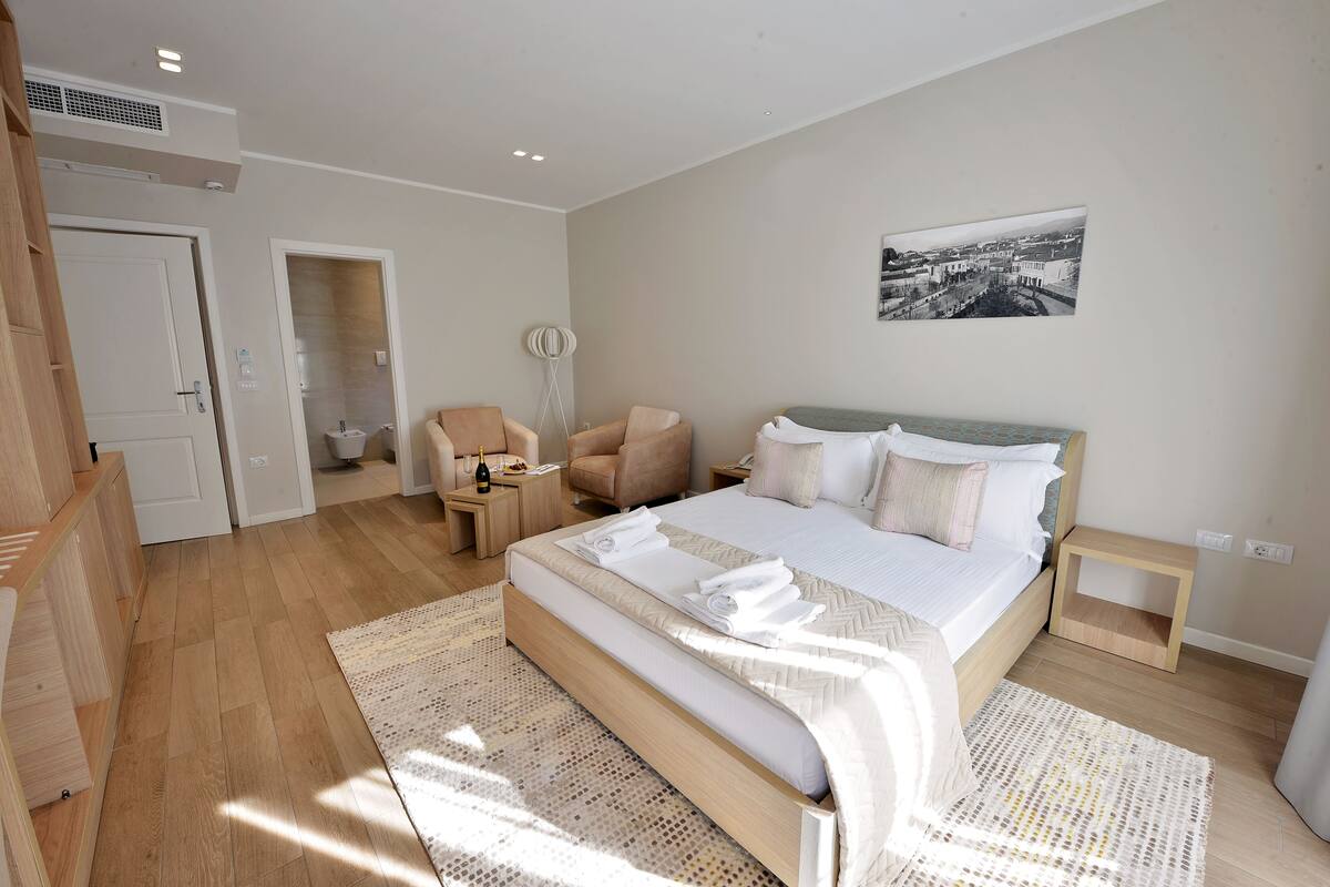 A modern bedroom with a large bed, a sitting area with chairs, a small table, and a picture on the wall.
