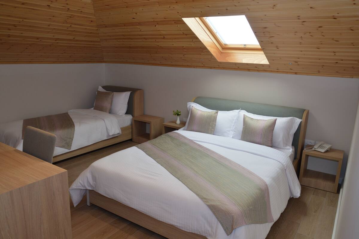A bedroom with two beds, wooden headboards, a skylight, and a bedside telephone.