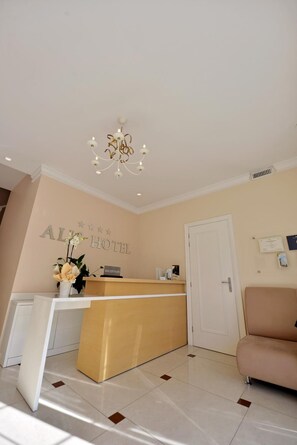 A hotel reception area with a reception desk, a chandelier, a reception sign, a reception counter, a sofa, and a door. - Alis Hotel (Shkodër)