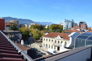 A cityscape with a prominent white building with a clock tower, surrounded by modern buildings and mountains in the background. - Alis Hotel (Shkodër)