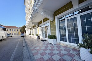 A hotel facade with large windows, a checkered pavement, and parked cars. - Alis Hotel (Shkodër)