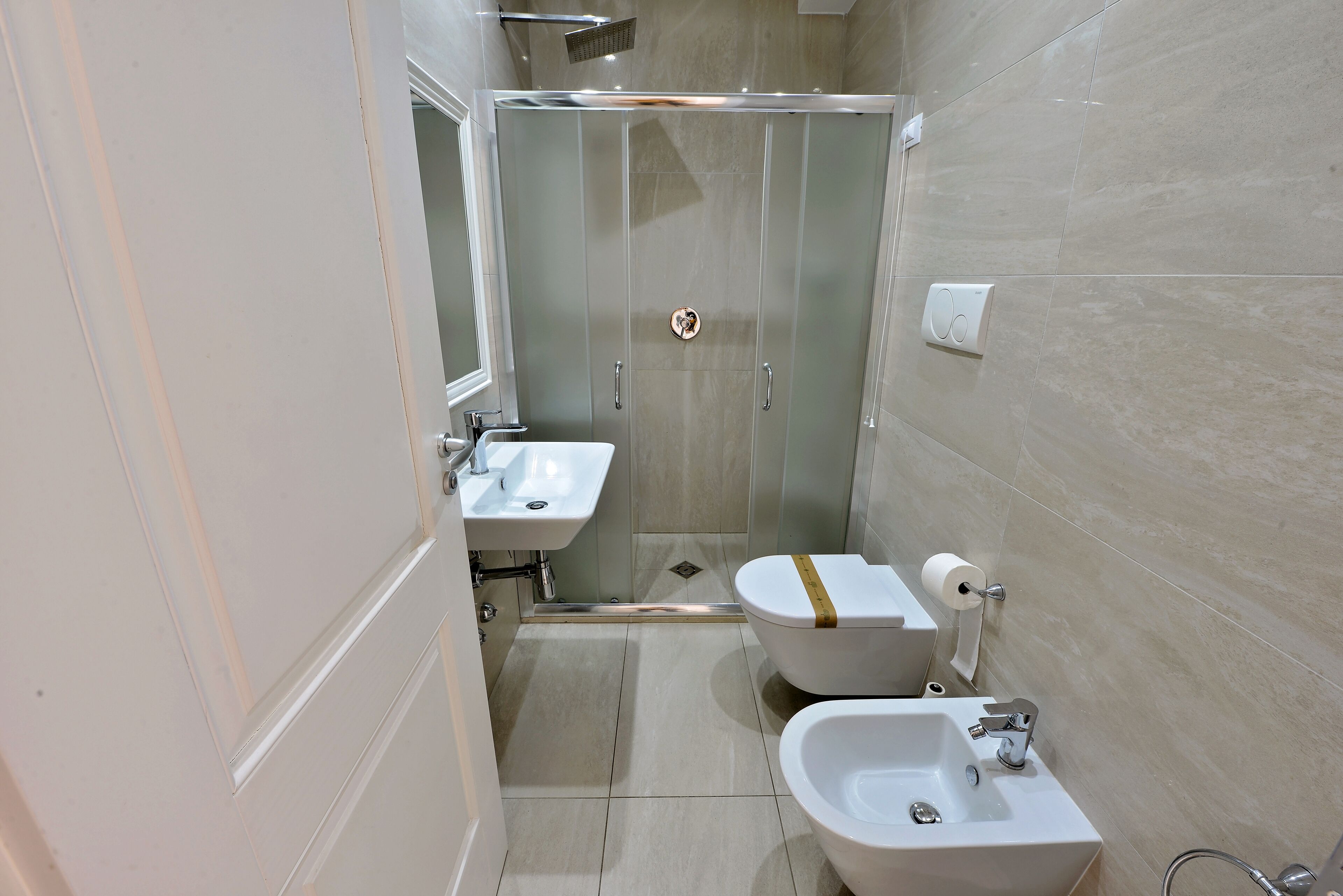 A modern bathroom with a glass-enclosed shower, a toilet, a bidet, and a sink.
