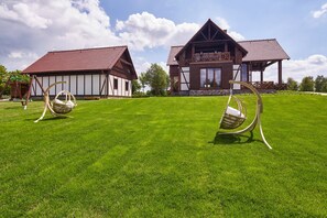 Une maison traditionnelle en bois, avec un toit recouvert de tuiles rouges, une pelouse bien entretenue et deux balançoires.