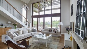 A spacious living room with a high ceiling, large windows, a staircase, and a fireplace. - Siedlisko 518 Wzgorza Dylewskie (Ostróda)