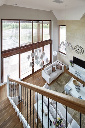 Un vaste espace de vie doté d’une grande fenêtre, d’un canapé blanc, d’un escalier en bois et d’un téléviseur à écran plat.