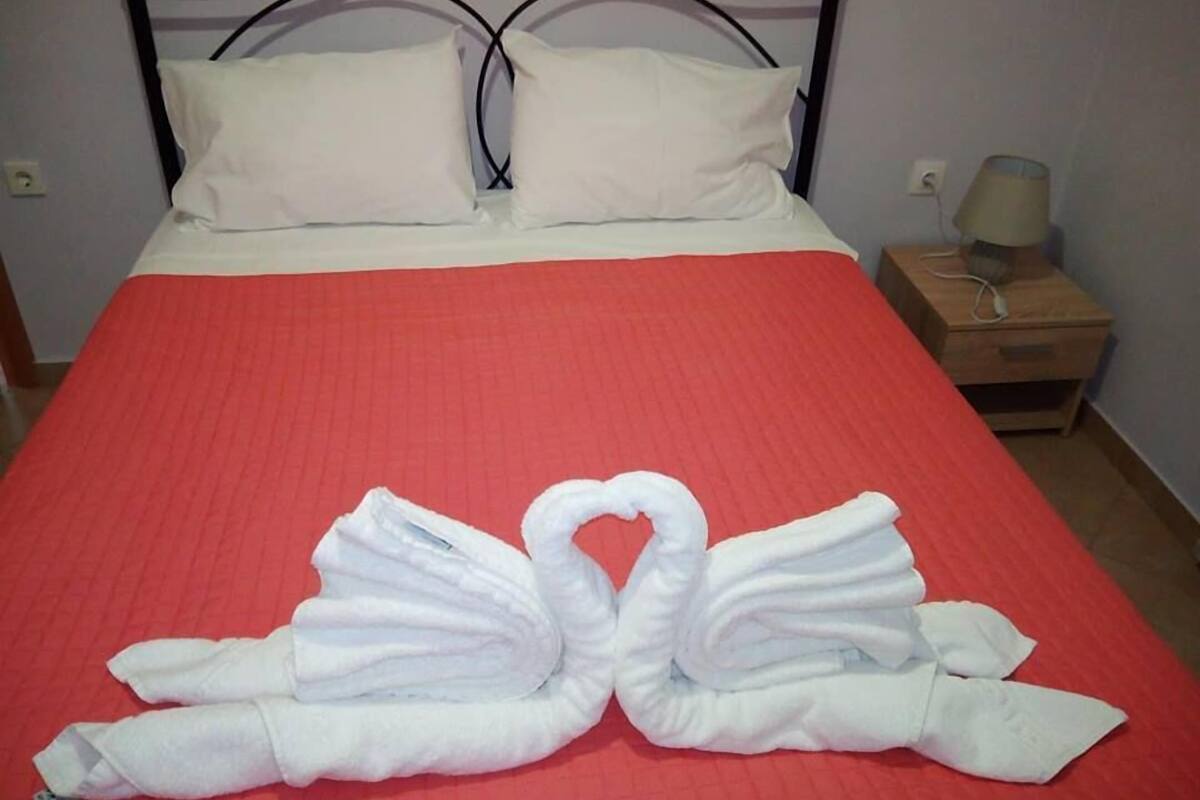 Un lit avec une couvre-lit rouge, des oreillers blancs et une disposition de serviettes en forme de cygnes.