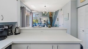 A modern kitchen with white cabinets, a coffee maker, and a view into the living area.