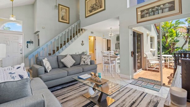 A spacious living room with a grey sofa, a glass coffee table, and a staircase leading to another level.