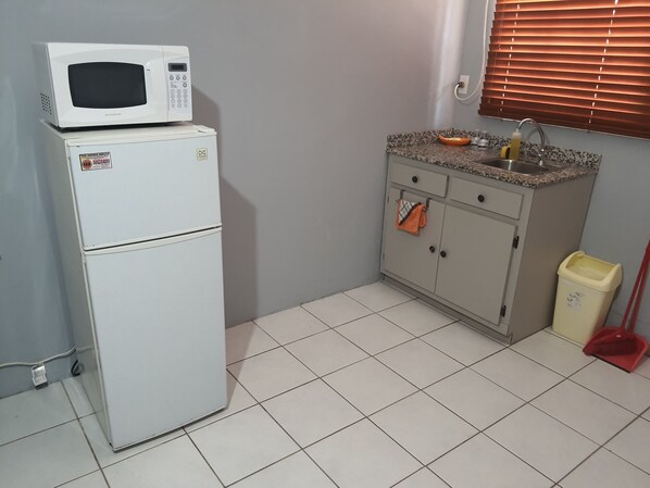 Una cocina compacta con un refrigerador blanco, un microondas, una encimera de granito, un lavamanos y una escoba.