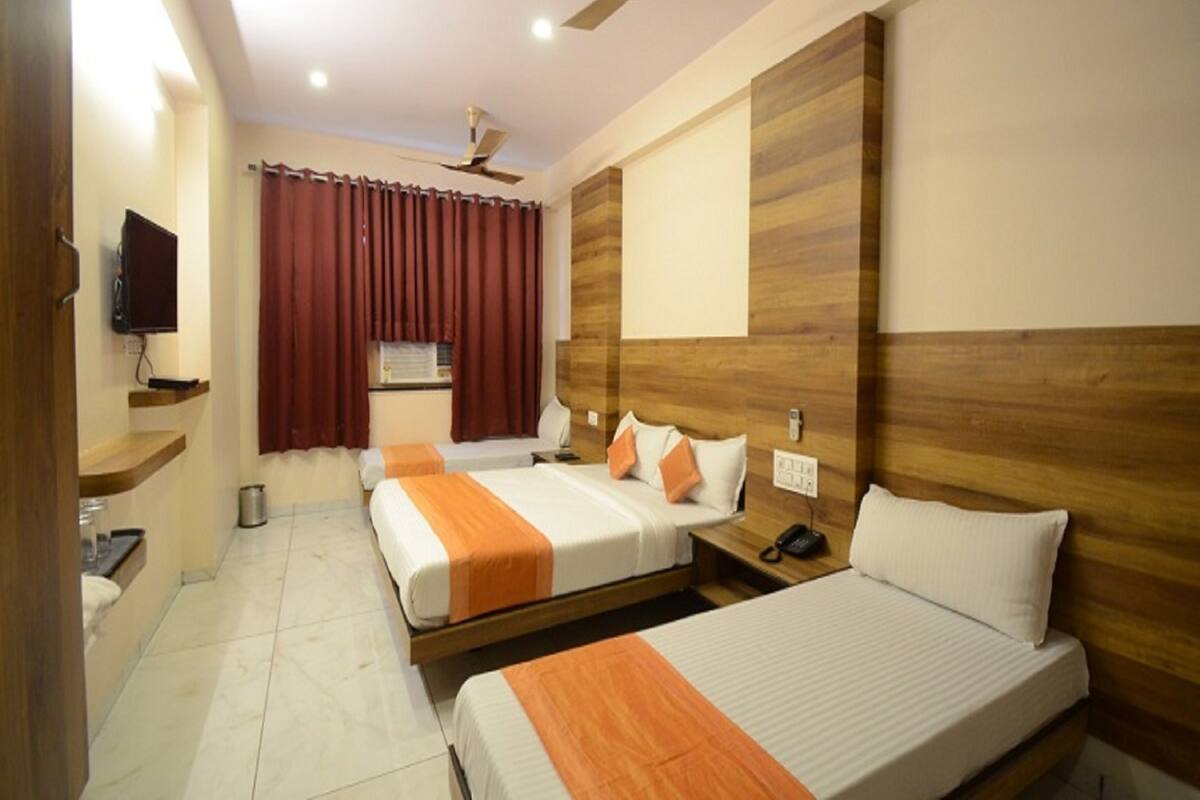 A hotel room with two beds, a TV, a ceiling fan, and a window with curtains.