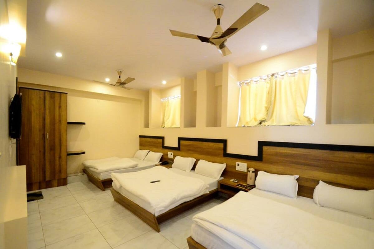 A hotel room with three single beds, a wooden wardrobe, a ceiling fan, and a window with curtains.