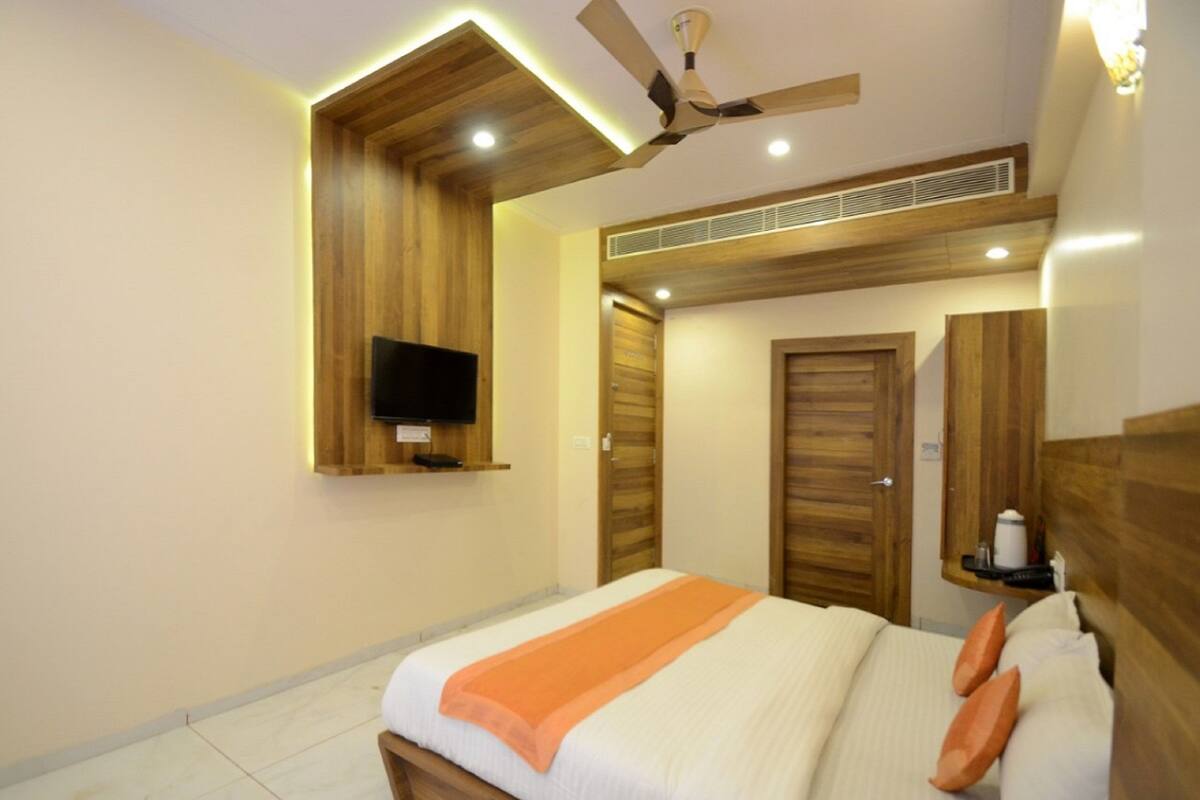A hotel room with a bed, a ceiling fan, a television mounted on the wall, and wooden doors.