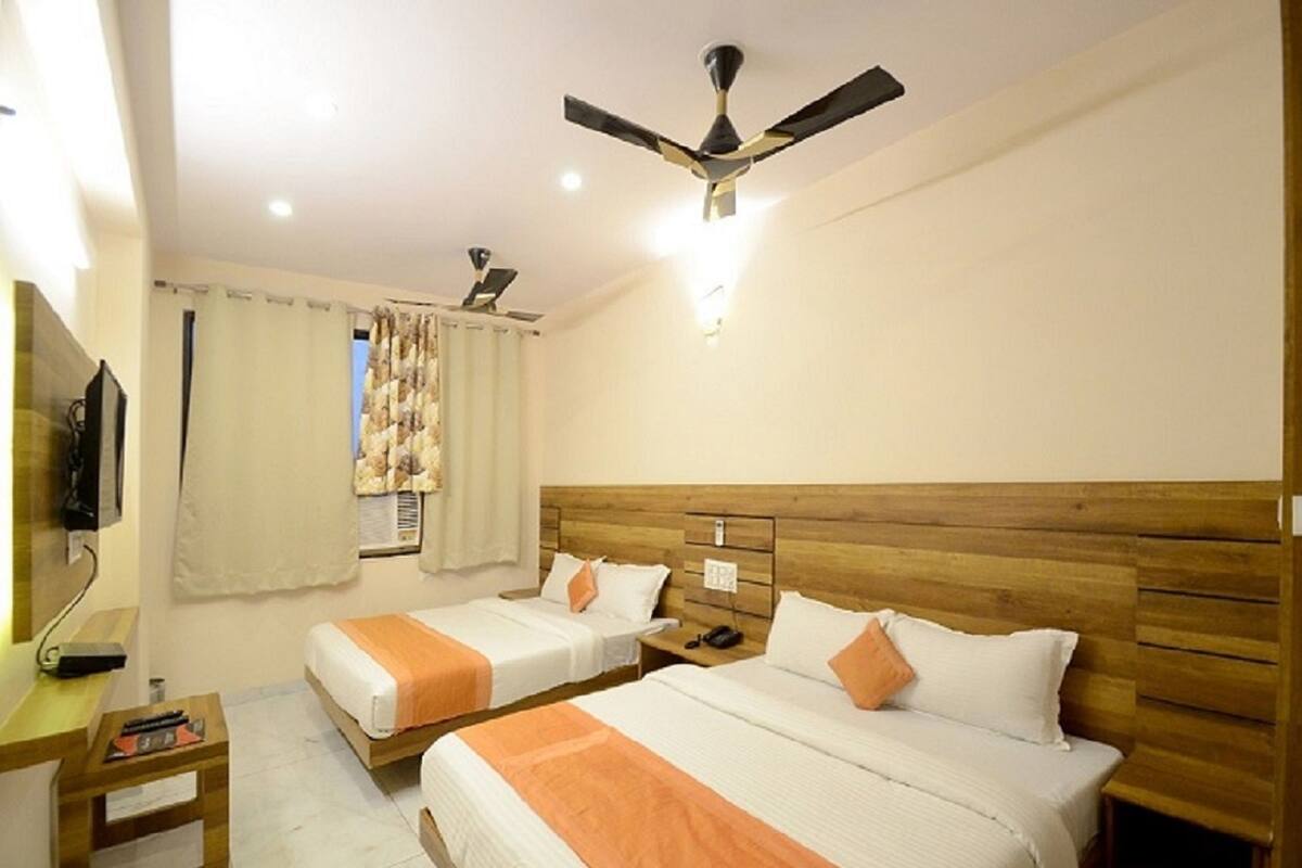 A hotel room with two beds, wooden headboards, a ceiling fan, a TV, and a bedside table.