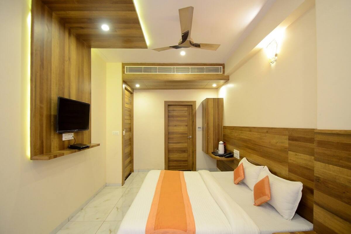 A modern bedroom with a bed, a TV mounted on a wooden shelf, a ceiling fan, and a wooden wardrobe.