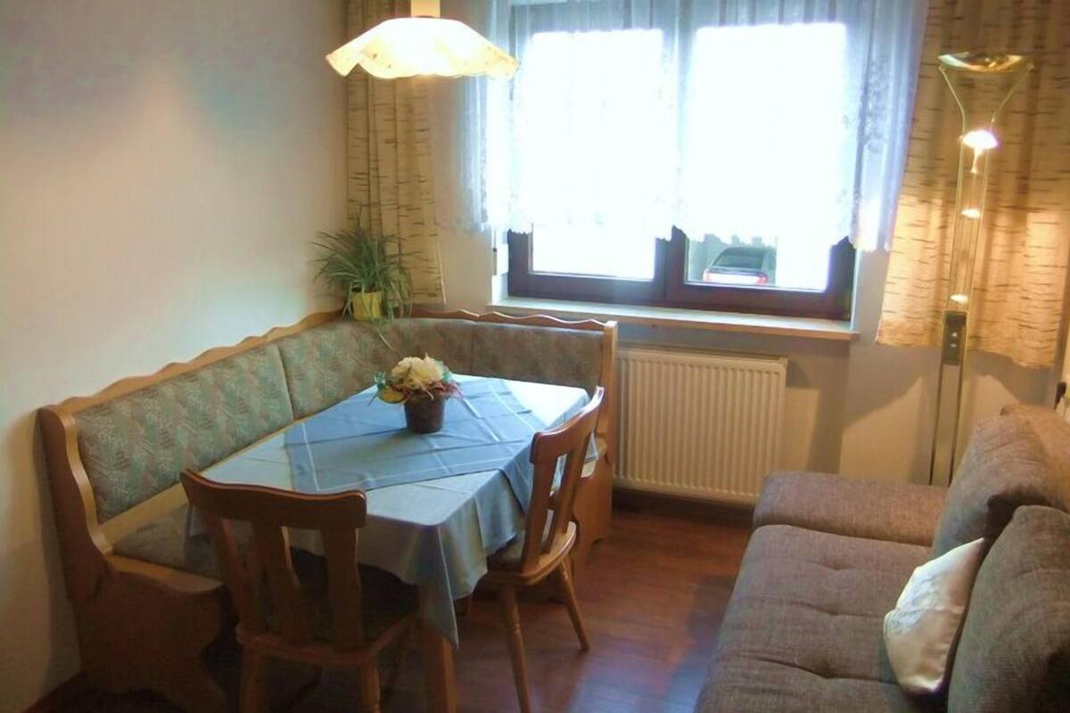 Ein Essbereich mit Tisch für zwei Personen, einer Bank und einem Fenster mit Vorhängen.