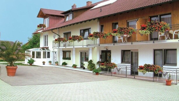 Un hotel de dos pisos con techo de tejas, balcones con jardineras y un patio empedrado.