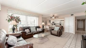 A spacious living room with a brown leather sofa, a glass coffee table, and a dining area with chairs.
