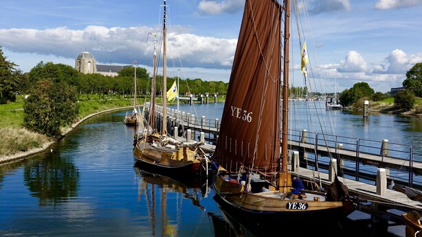 A river with boats docked at a pier, a bridge in the background, and a building with a dome.