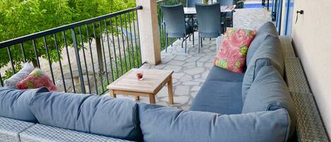 A balcony with a grey sofa, a small wooden table, and a glass of red drink.