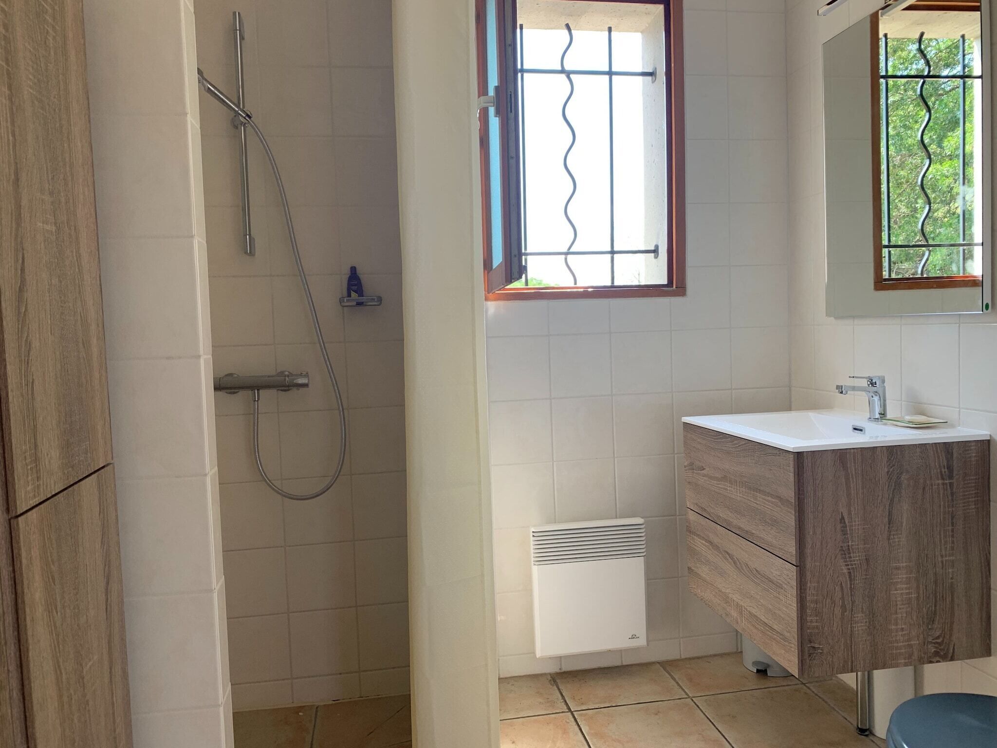 Een badkamer met een douche, wastafel en een raam met uitzicht op groen.
