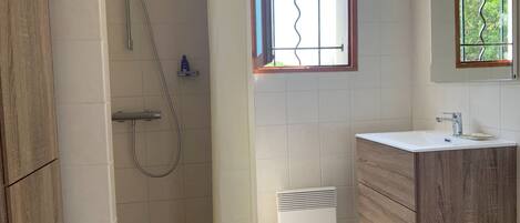 Een badkamer met een douche, wastafel en een raam met uitzicht op groen.